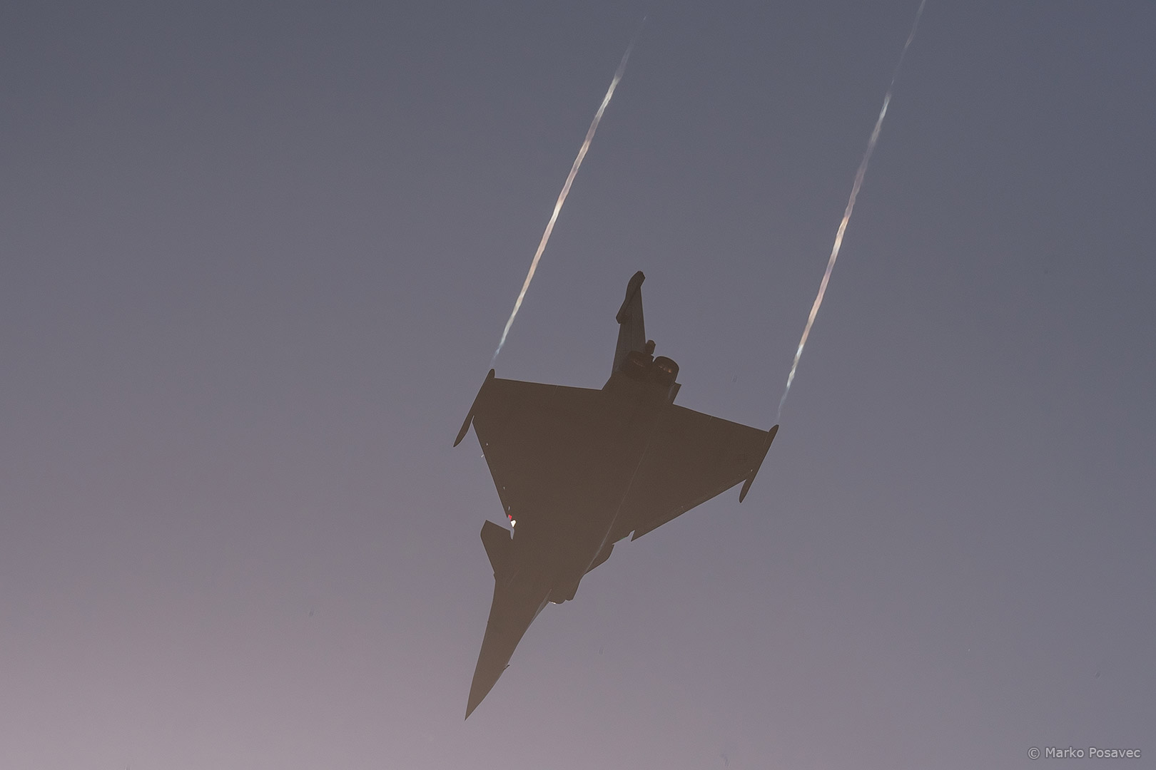 Silueta lovačkog aviona Rafale s vidljivim, blago šarenim vrpcama kondenzacije iza vrškova krila