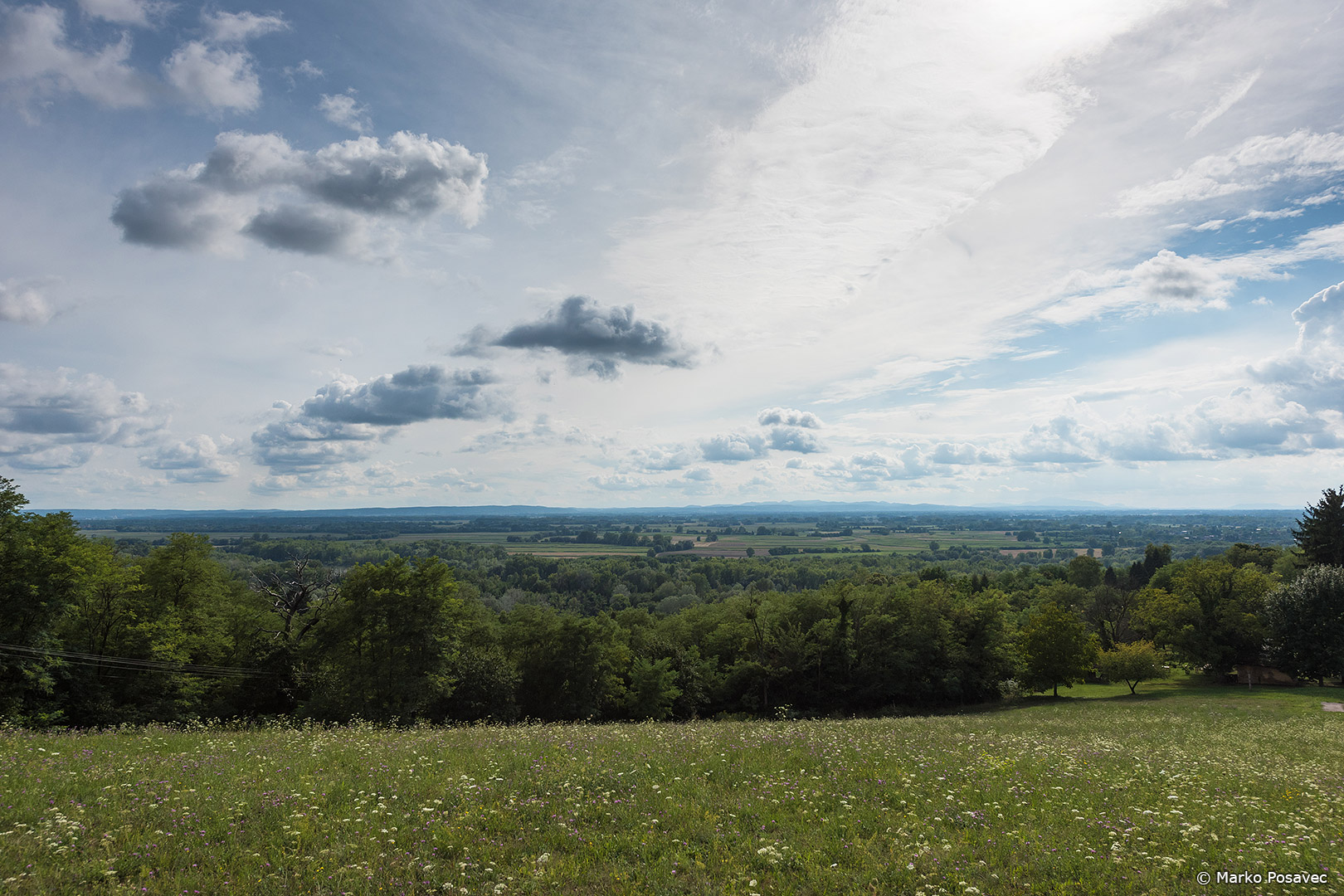 Pogled na ravničarski kraj s travnatog brda pod poluoblačnim nebom