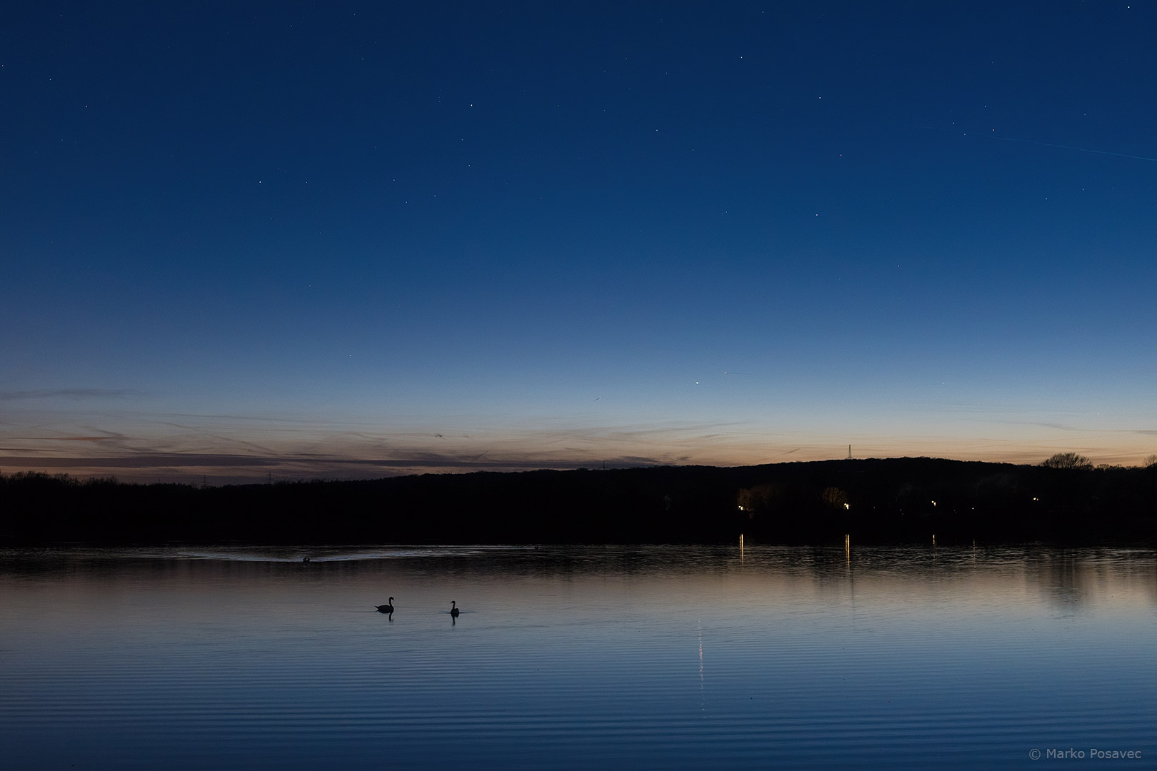 Jezero s labudovima u sumrak ispod neba na kojem se vide prve zvijezde