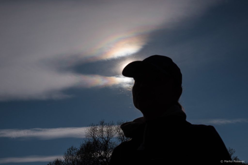 Silueta osobe s kapom koja zaklanja Sunce oko kojega su raznobojne šare na oblacima