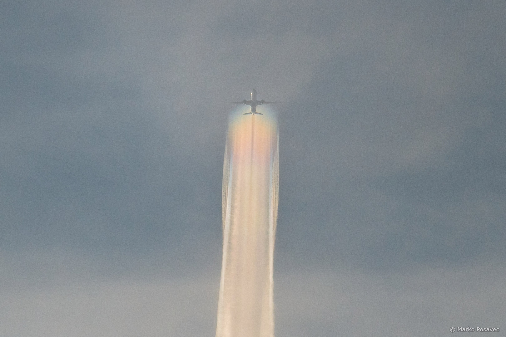 Avion u daljini koji ostavlja širok trag u duginim bojama