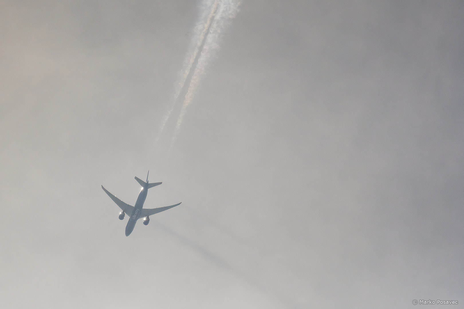 Silueta Boeinga 777 s dvije tamne linije koje se pružaju dolje desno od zrakoplova